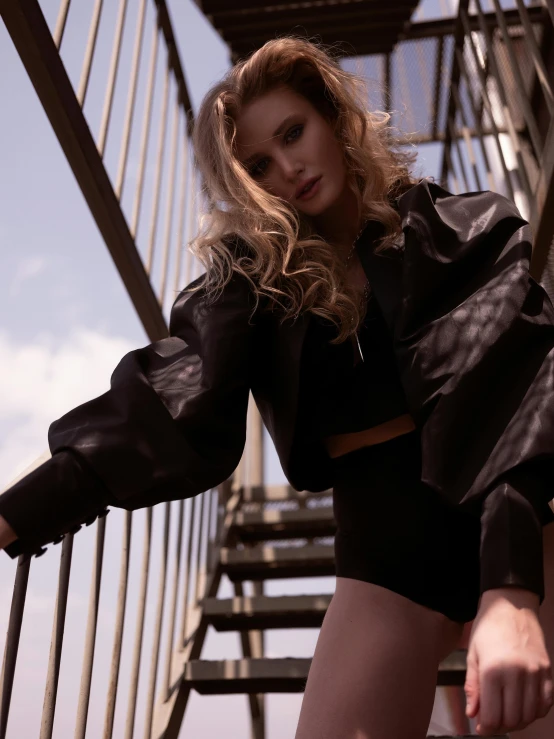 a woman standing on a set of stairs, an album cover, by Emma Andijewska, unsplash, happening, leather bomber jacket, wearing a sexy cropped top, in a rooftop, voluminous sleeves