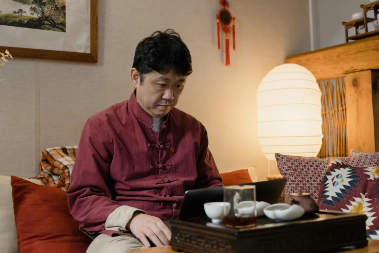 a man sitting on a couch using a laptop, shin hanga, traditional chinese clothing, sen no rikyu, reflecting, 2019 trending photo