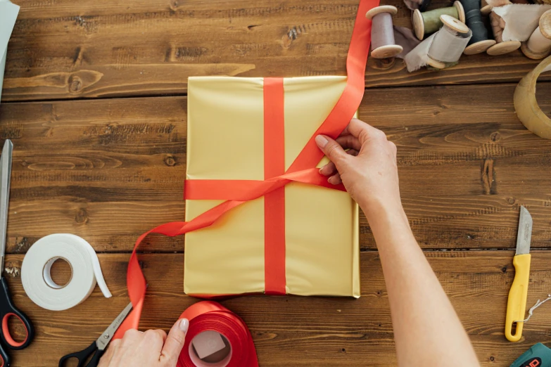 a person wrapping a gift with a red ribbon, pexels contest winner, arts and crafts movement, yellow, vinyl material, bespoke, rectangle