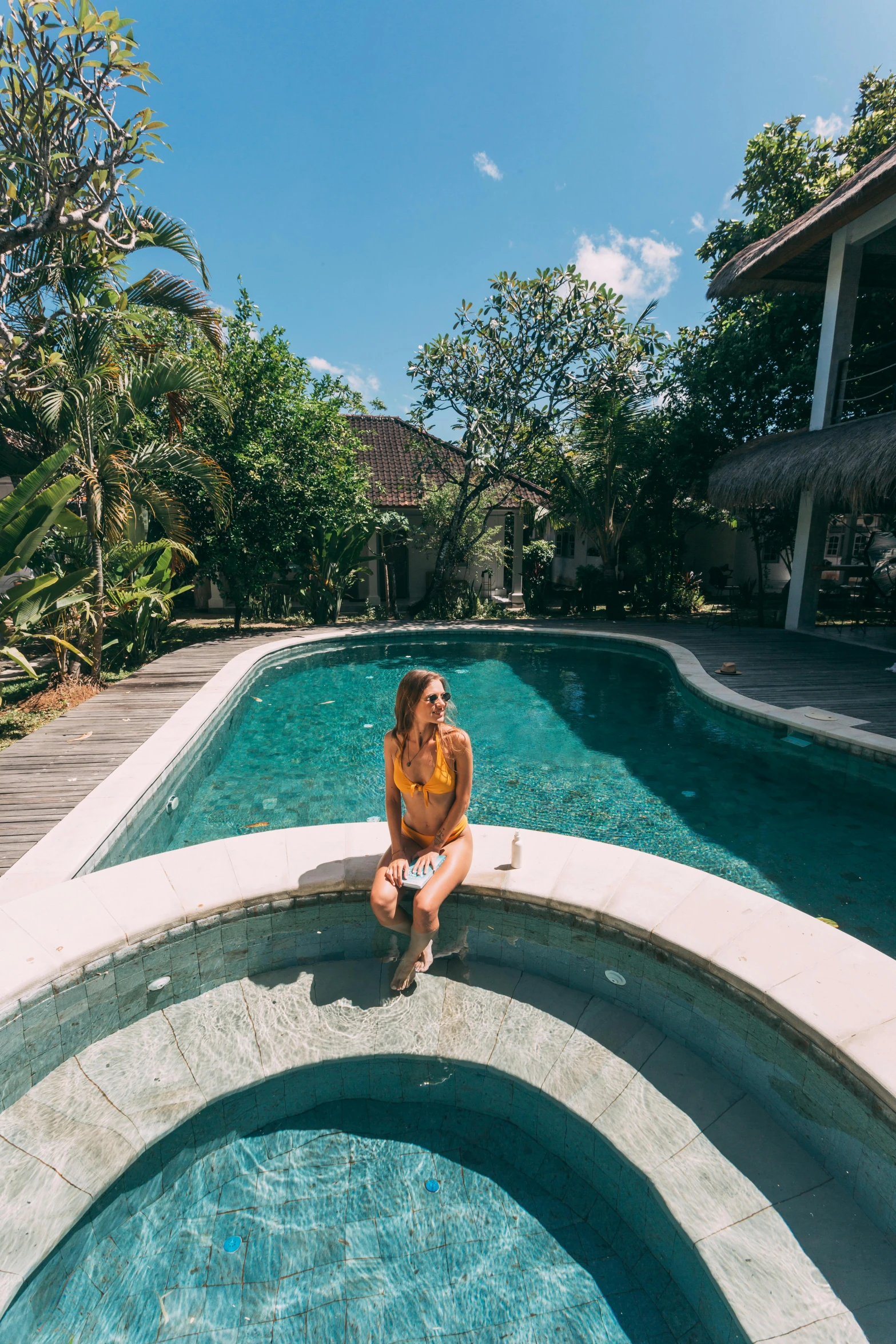 a woman sitting on the edge of a swimming pool, above lush garden and hot spring, chill vibes, bali, blue skies