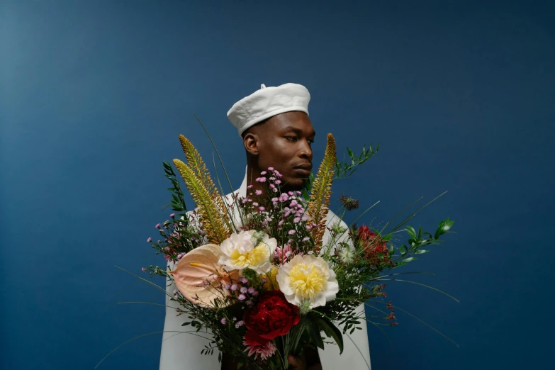 a man holding a bouquet of flowers in front of a blue wall, an album cover, inspired by François Boquet, unsplash, wearing white chef hat, black man, portrait n - 9, close - up photograph