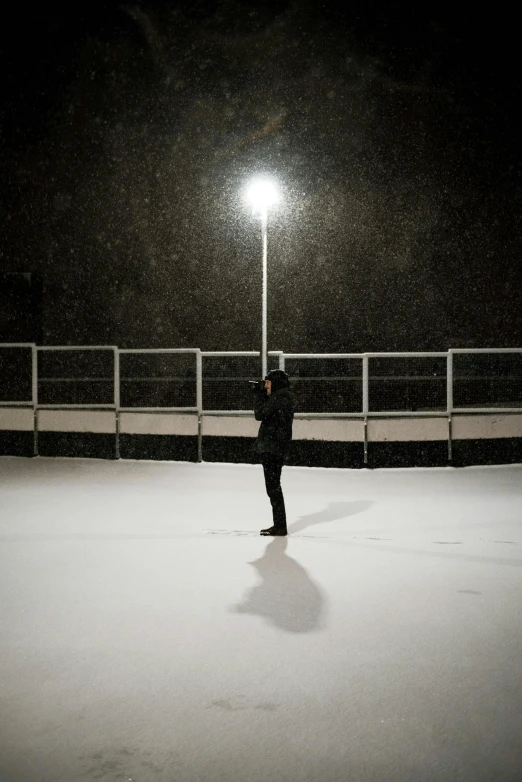 a person standing in the snow under a street light, on a football field, dark dance photography aesthetic, looking sad, at a skate park