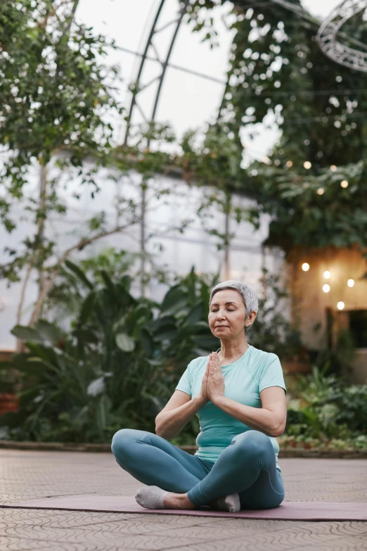 a woman sitting in the middle of a yoga pose, large plants in the background, older woman, enlightening, centered in image