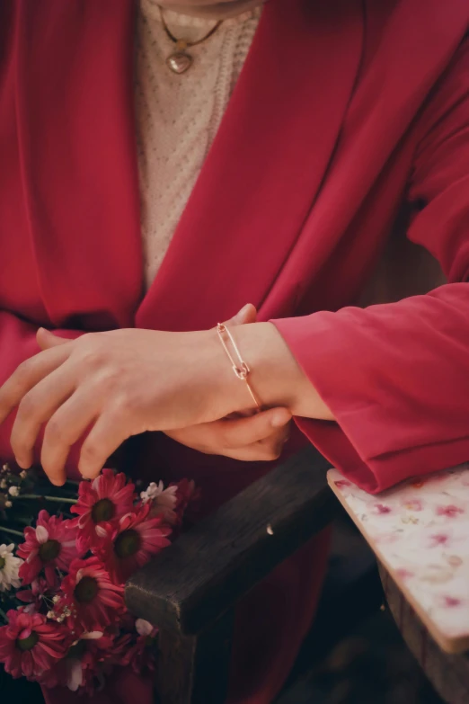 a woman sitting on a bench holding a bouquet of flowers, by Emma Andijewska, gold bracelet, detail shot, pink, fine details. red