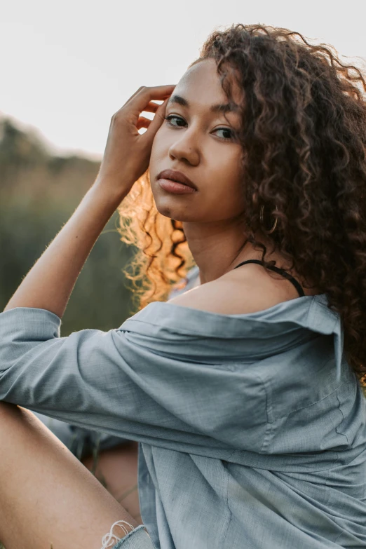 a woman sitting on top of a lush green field, a portrait, trending on pexels, renaissance, curls hair, wearing a light blue shirt, mixed race woman, looking seductive