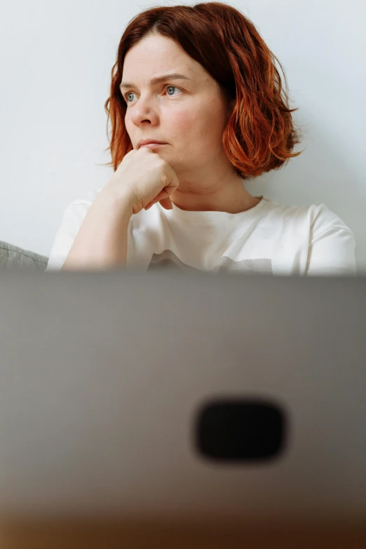 a woman sitting in front of a laptop computer, inspired by Louisa Matthíasdóttir, pexels, short redhead, distant thoughtful look, bottom angle, low quality photo