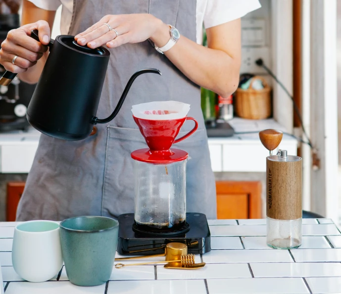 a woman pours a cup of coffee in a kitchen, a still life, by Julia Pishtar, aussie baristas, cone shaped, slightly red, full device