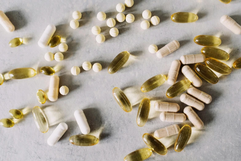 a table topped with lots of pills and capsules, by Jessie Algie, trending on pexels, renaissance, white and yellow scheme, skincare, on grey background, natural materials