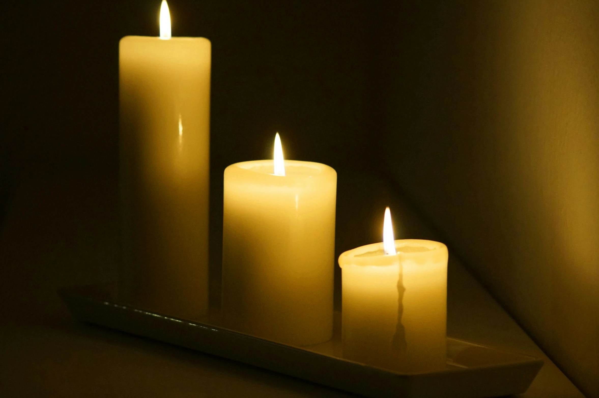 three lit candles sit on a tray in the dark, soft white glow, made of glowing wax and ceramic, mesmerising, ivory