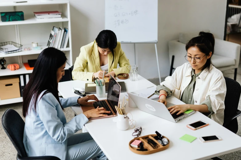 a group of people sitting around a table with laptops, trending on pexels, three women, white wall coloured workshop, asian women, background image