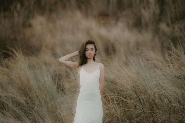 a woman standing in a field of tall grass, unsplash, minimalism, wearing ivory colour dress, asian girl, photoshoot for skincare brand, beaches