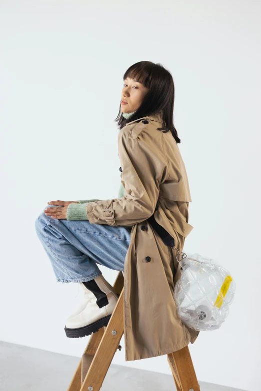 a woman sitting on top of a wooden step ladder, by Miyamoto, unsplash, visual art, wearing a plastic garbage bag, light brown trenchcoat, model エリサヘス s from acquamodels, burberry