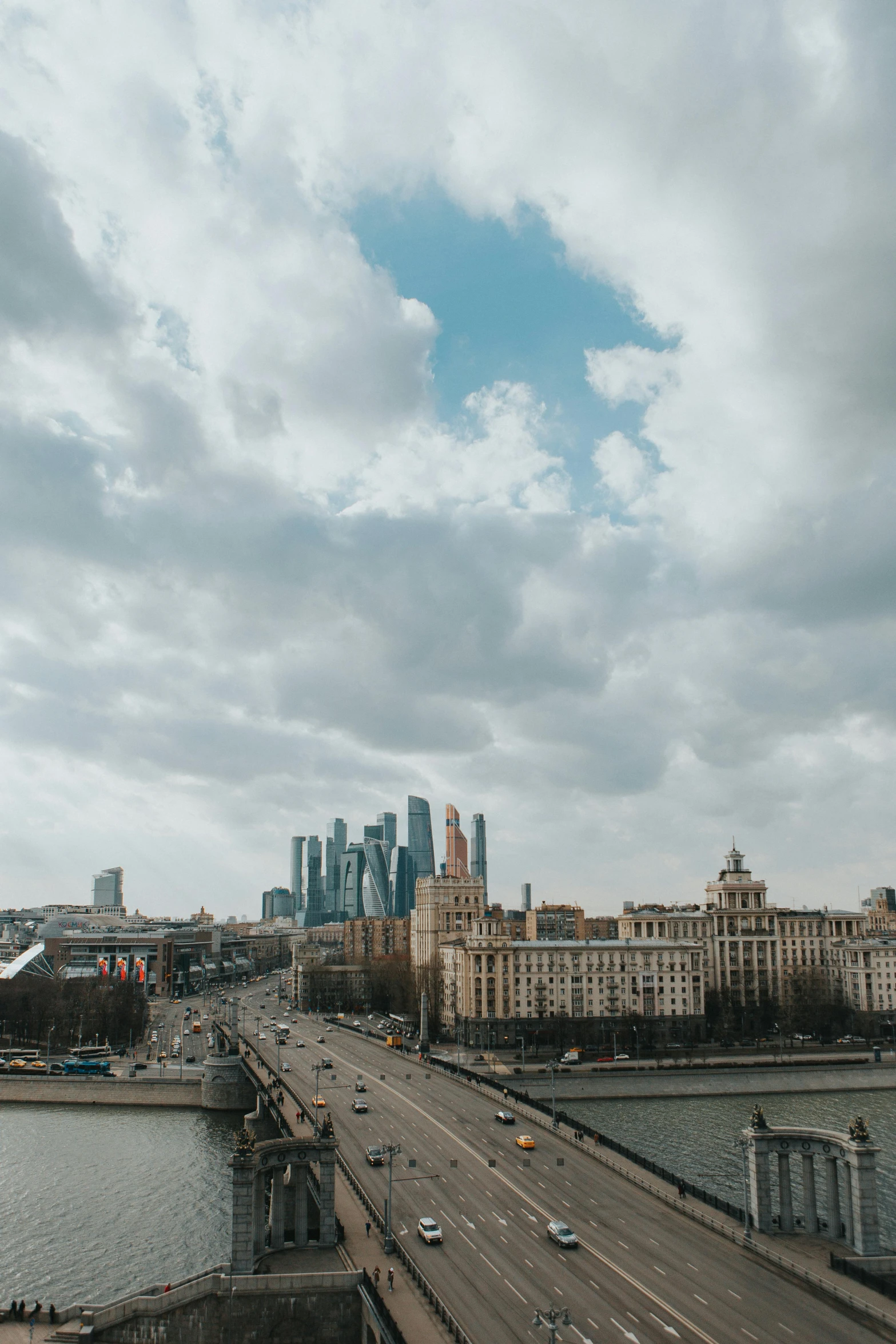 a bridge over a body of water with a city in the background, by Serhii Vasylkivsky, pexels contest winner, socialist realism, skyline view from a rooftop, light blue sky with clouds, street of moscow, on a gray background