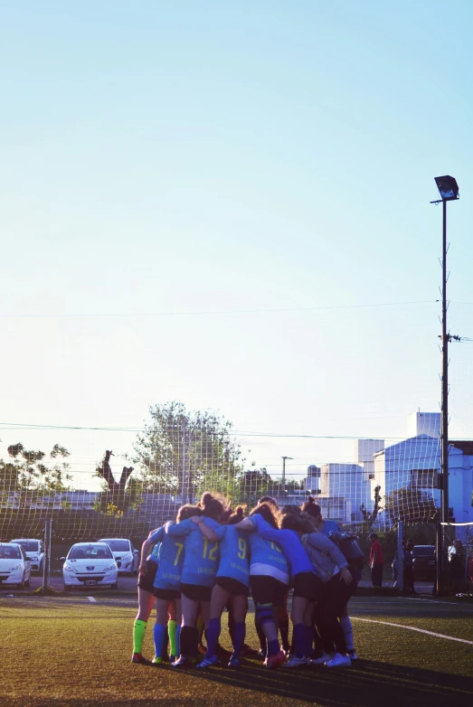 a group of people standing on top of a soccer field, on a parking lot, facing away, light blues, wearing a volleyball jersey