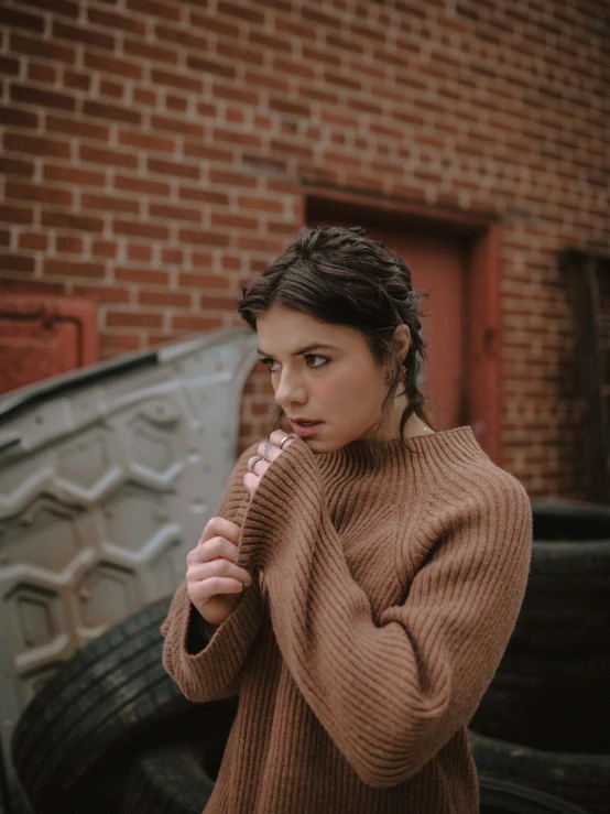 a woman standing next to a pile of tires, inspired by Elsa Bleda, trending on pexels, renaissance, he is wearing a brown sweater, her hair pinned up, soft portrait shot 8 k, with brown hair