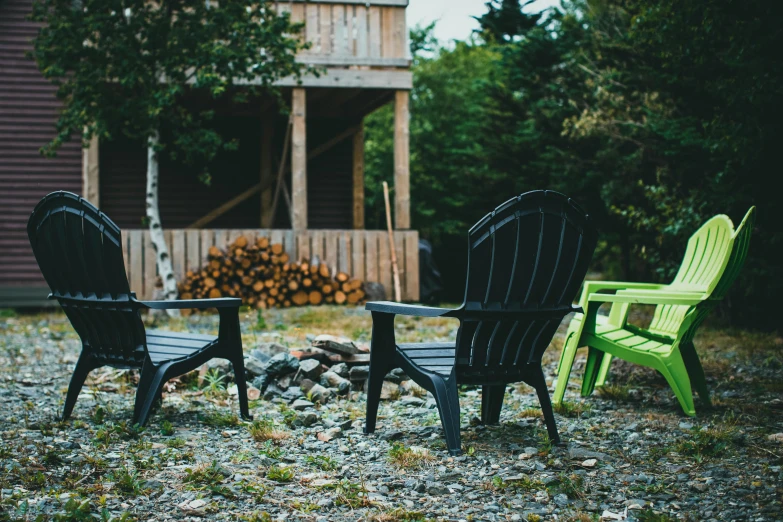 a couple of lawn chairs sitting next to a fire pit, by Jessie Algie, unsplash, private press, several cottages, haida gwaii, green and black color scheme, plastic chair