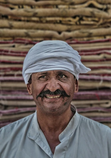 a man standing in front of a pile of carpet, by Peter Churcher, pexels contest winner, with a orientalist smileful face, oman, milkman, detailed face with moustache
