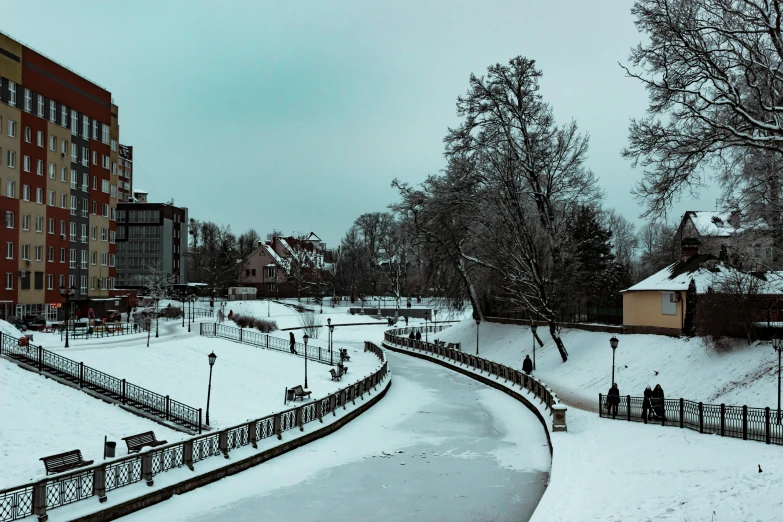 a city street covered in snow next to tall buildings, a photo, by Tamas Galambos, pexels contest winner, hurufiyya, in a park and next to a lake, in legnica, thumbnail, kramskoi 4 k