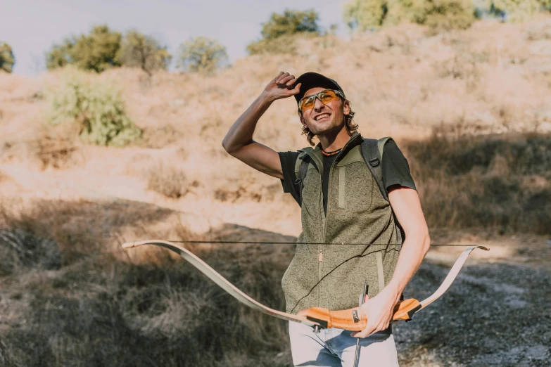 a man standing in a field holding a bow and arrow, pexels contest winner, modern casual clothing, avatar image, arrendajo in avila pinewood, technical vest
