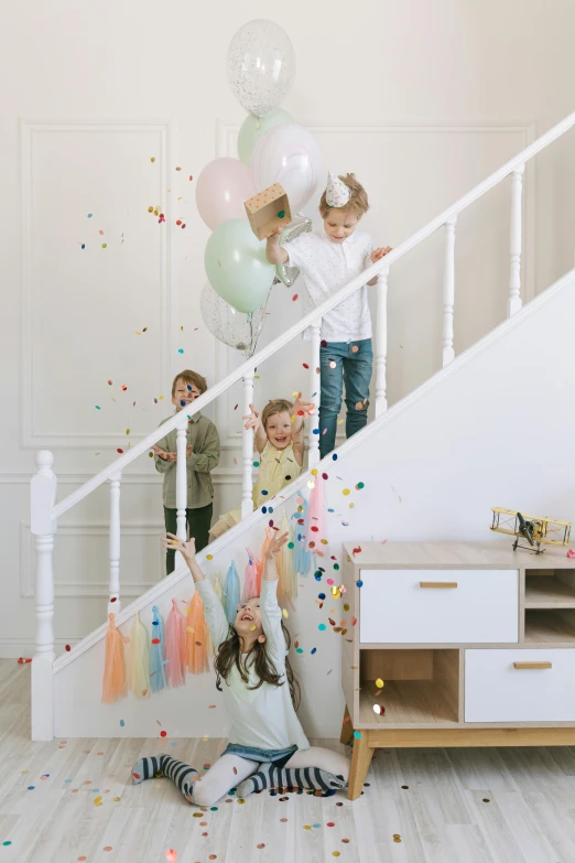 a group of children playing with balloons and confetti, 1 staircase, light colours, lifestyle, dwell
