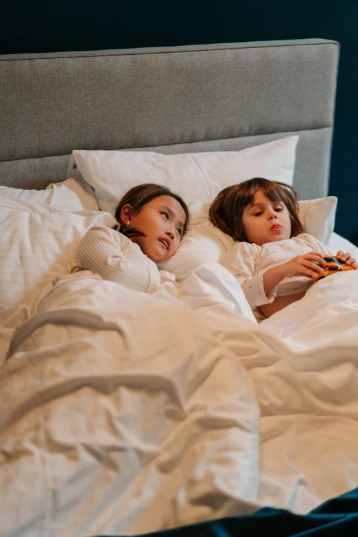a couple of kids laying on top of a bed, by Adam Marczyński, pexels, fine art, snacks, emma watson in bed, hotel, annoyed