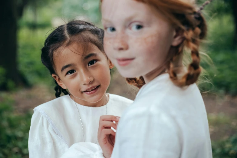 a couple of young girls standing next to each other, inspired by Kate Greenaway, pexels contest winner, pre-raphaelitism, ginger hair with freckles, young asian girl, wearing white clothes, slide show