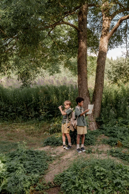 a couple of kids standing next to a tree, a picture, by Jan Tengnagel, pexels, visual art, summer camp, in spain, reading under a tree, scout boy
