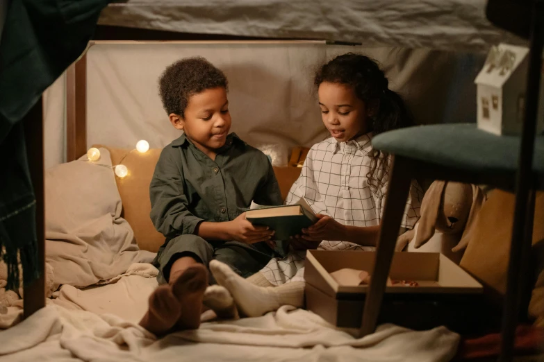 a couple of kids sitting on top of a bed, a storybook illustration, by Adam Marczyński, pexels contest winner, cardboard tunnels, ( ( dark skin ) ), snacks, interior of a tent