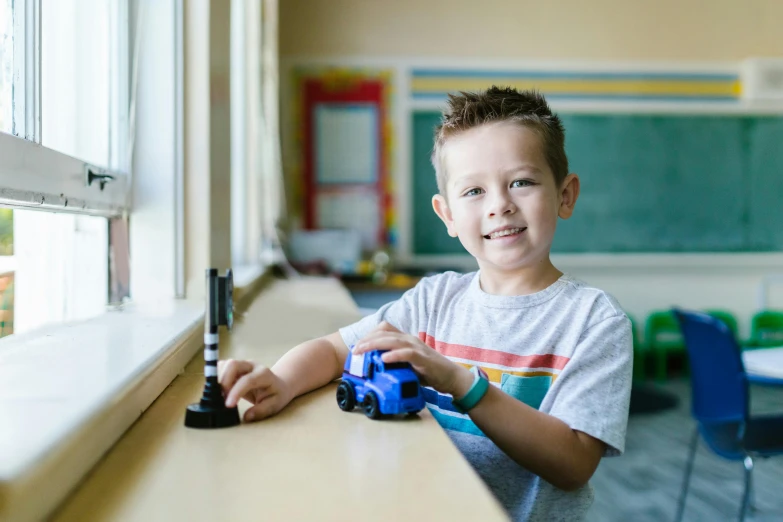 a little boy that is sitting in front of a window, a picture, smiling, prosthetic arm, toy photo, student