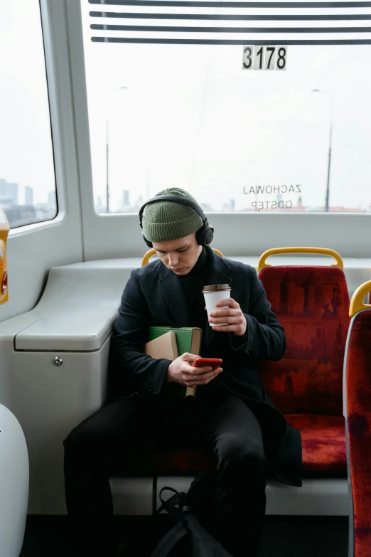 a man sitting on a bus looking at his cell phone, an album cover, trending on unsplash, drinking tea, headphones on head, julian ope, human staring blankly ahead