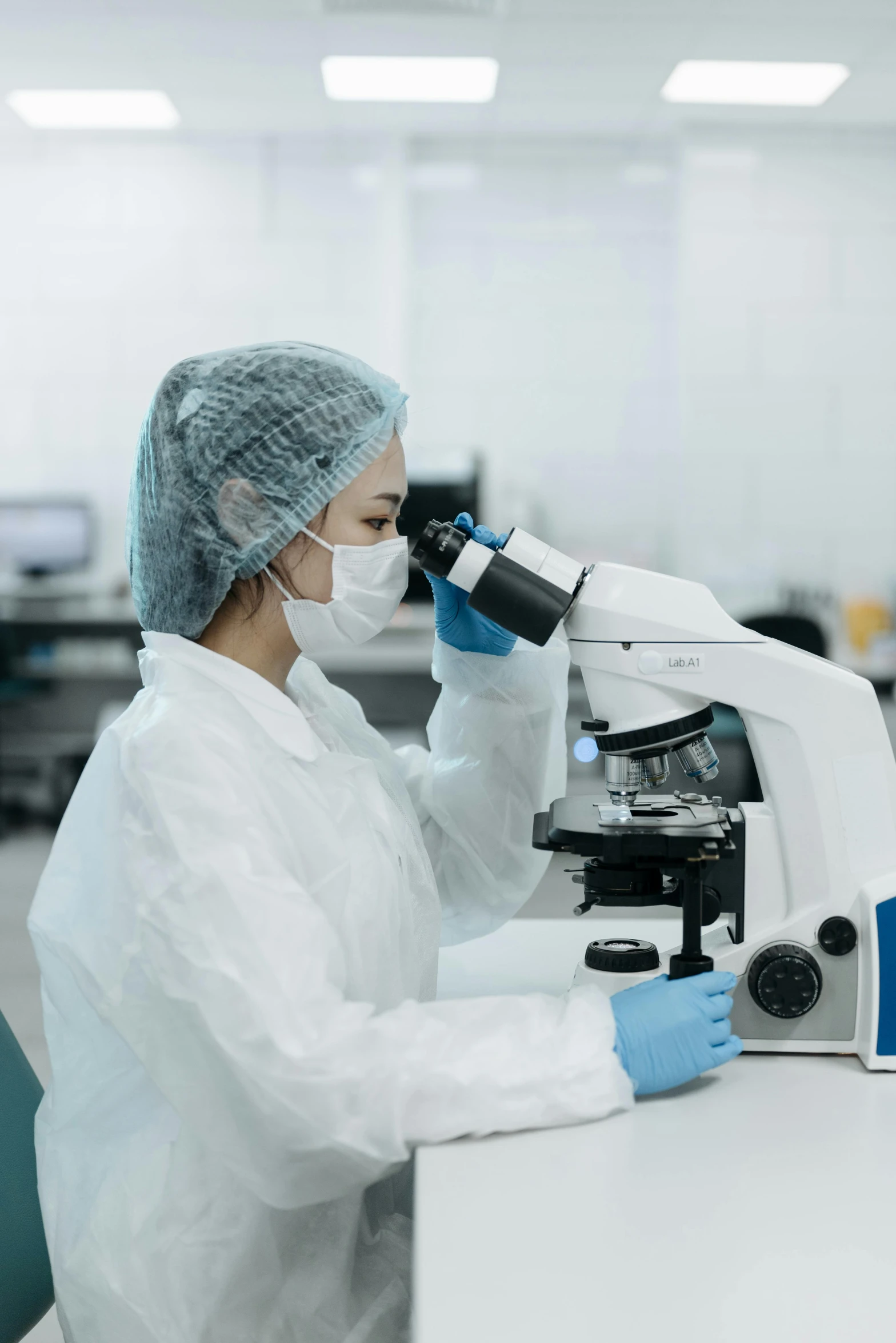 a woman in a lab coat using a microscope, a microscopic photo, shutterstock, hazmat suits, 15081959 21121991 01012000 4k, surgical gown and scrubs on, instagram photo