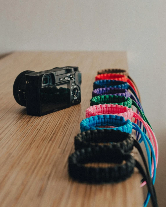 a camera sitting on top of a wooden table, bracelets, electric colours, unsplash transparent, braided cable
