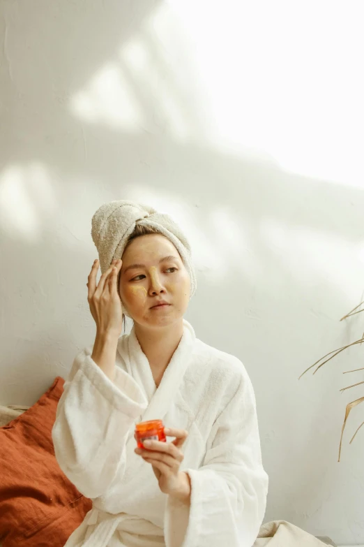 a woman sitting on a bed holding an apple, inspired by Li Di, trending on pexels, shower cap, asian face, white and orange, bathrobe