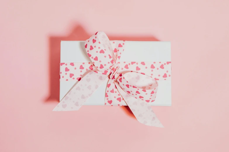 a white gift box with a pink bow on a pink background, by Eden Box, pexels contest winner, delicate patterned, chocolate, thumbnail, hearts