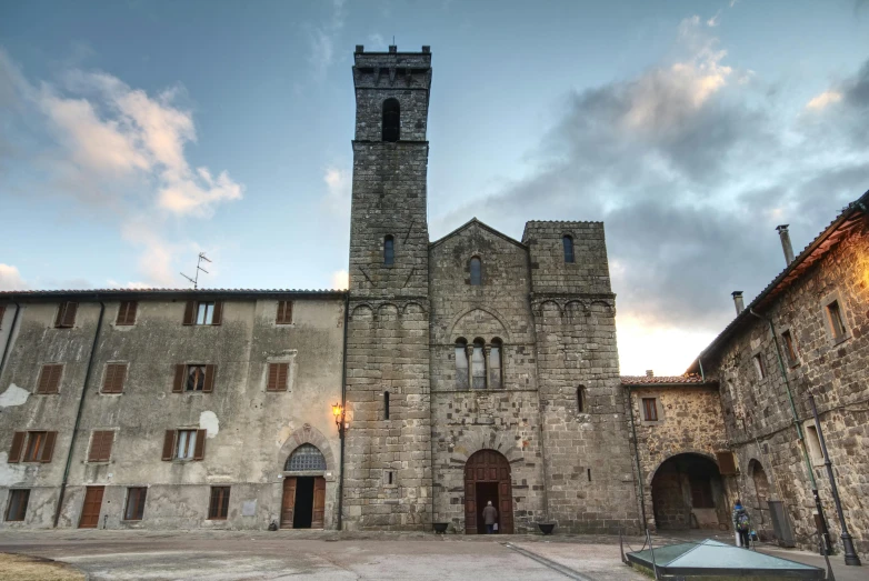 a large stone building with a clock tower, an album cover, by Carlo Martini, romanesque, village, at twilight, ground-level view, square