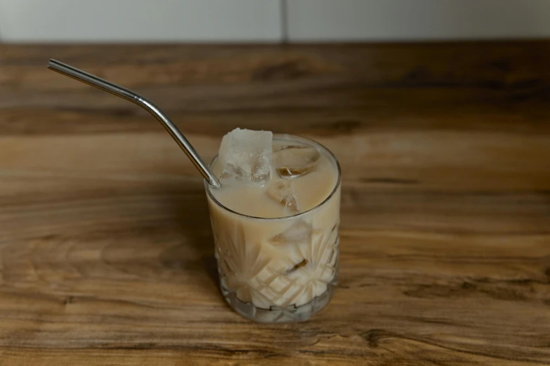 a glass filled with ice sitting on top of a wooden table, cream, spoon placed, jackstraws, bespoke