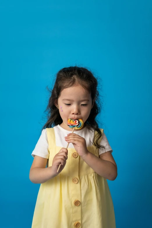 a little girl in a yellow dress eating a lollipop, inspired by Hikari Shimoda, pexels contest winner, blue, 9 0 mm studio photograph tiny, 12, multi colored