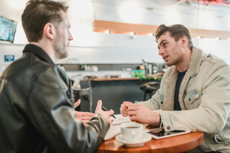 two men sitting at a table having a conversation, lachlan bailey, coffee shop, convincing, liam brazier