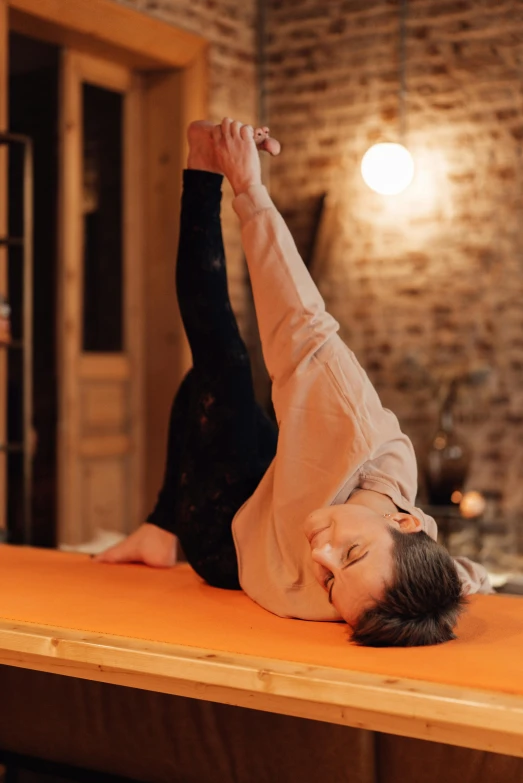 a woman doing a yoga pose on an orange mat, a picture, by Anna Haifisch, trending on pexels, arabesque, on wooden table, low ceiling, thumbnail, low quality photo