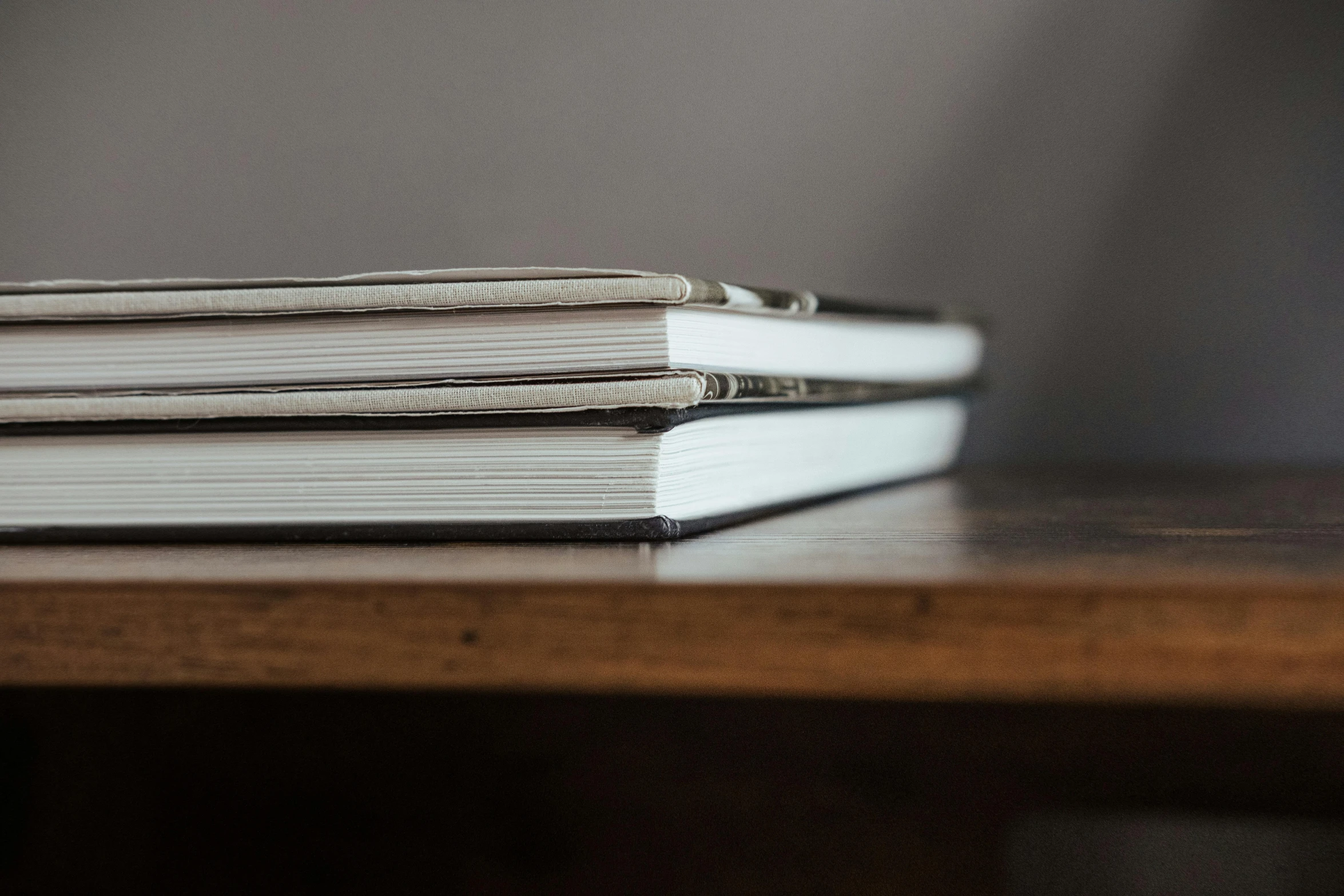 a stack of books sitting on top of a wooden table, an album cover, by Carey Morris, unsplash, private press, grey, soft light from the side, close up shots, bespoke