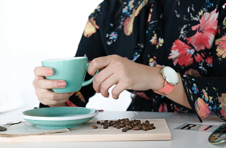 a woman sitting at a table with a cup of coffee, a still life, inspired by Natasha Tan, trending on unsplash, wearing a watch, turquoise pink and green, aussie baristas, holding arms on holsters