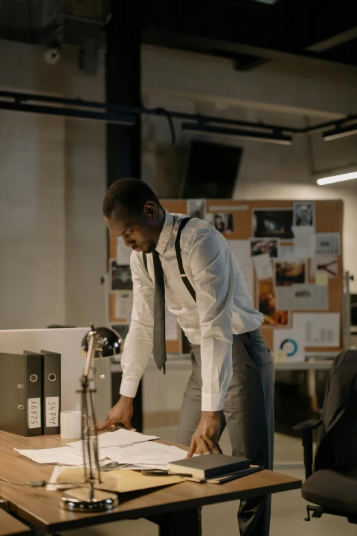 a man leaning over a desk in an office, pexels contest winner, happening, award winning movie still, black man, standing posture, papers on table