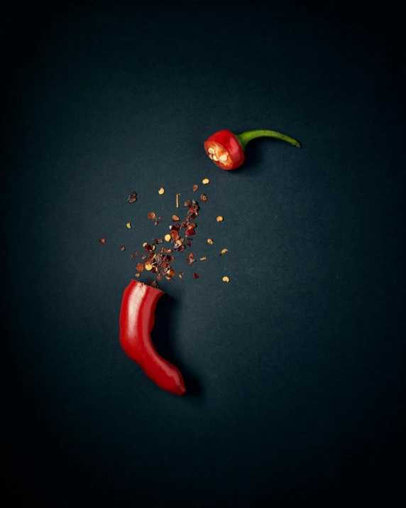 two chili peppers next to each other on a black surface, a picture, by Adam Marczyński, pexels contest winner, made of food, clemens ascher, food particles, crimson fork