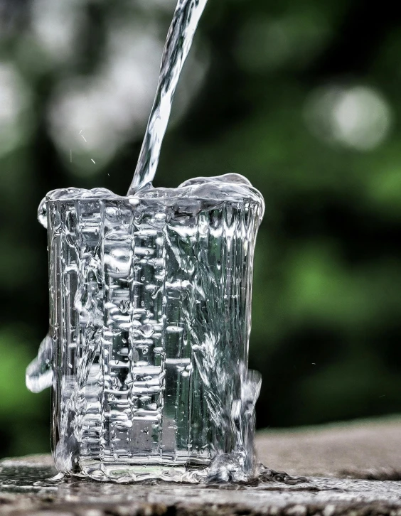 a glass filled with water sitting on top of a wooden table, by Cherryl Fountain, unsplash, renaissance, closeup of magic water gate, promo image, made of ice, high angle close up shot