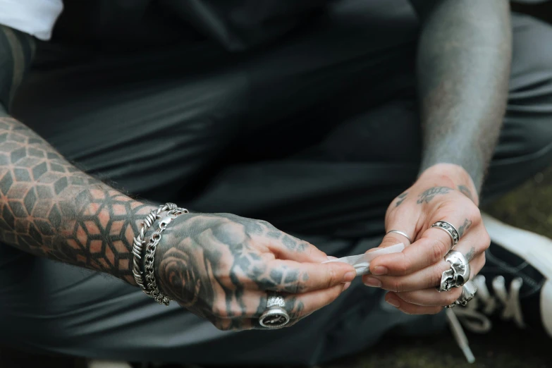 a close up of a person holding a cell phone, a tattoo, trending on pexels, silver bracelets, praying with tobacco, tattooed man, 7 0 mm photo