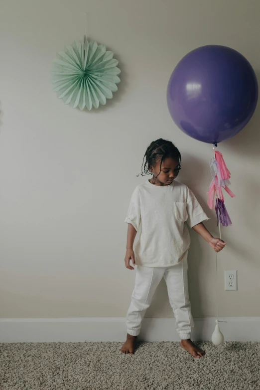 a little girl standing in front of a purple balloon, in a room, wearing off - white style, ( ( dark skin ) ), portrait featured on unsplash