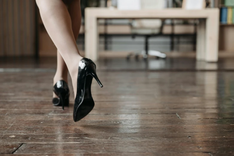 a woman in high heels walking across a wooden floor, trending on pexels, arabesque, dressed in black leather, flirting, performance, professionally made