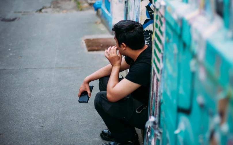 a man sitting on the side of a street talking on a cell phone, pexels contest winner, hunched over, asian male, background image, she's sad