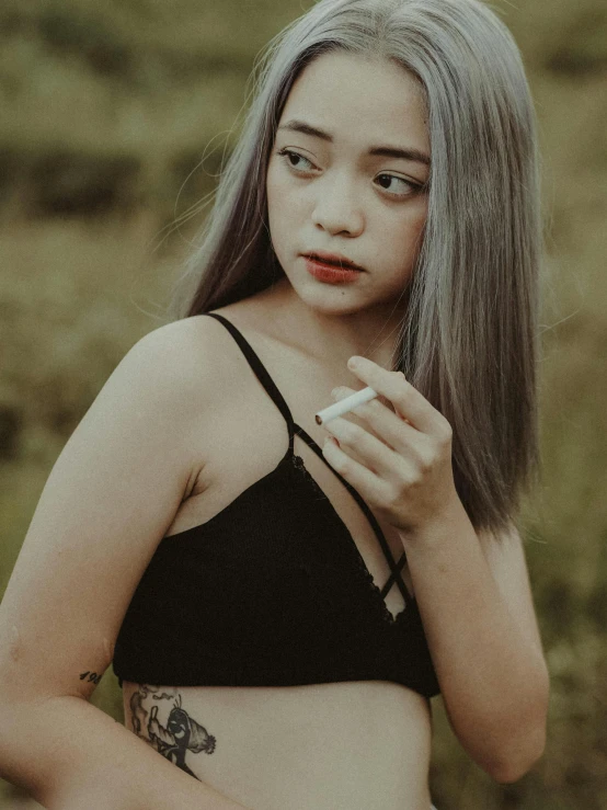 a woman standing in a field holding a cigarette, trending on pexels, with grey skin, asian girl, bralette, close up portrait photo