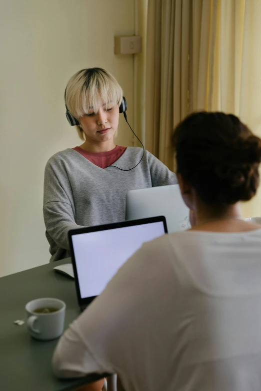 a couple of people sitting at a table with laptops, by artist, trending on pexels, wearing a headset, blonde women, séance, slightly minimal